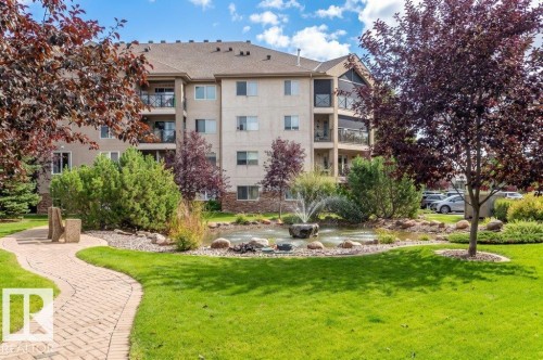 Manicured lawn with a winding paver pathway, decorative pond with a water feature, and mature landscaping - #203 8912 156 St Nw, Edmonton, AB 