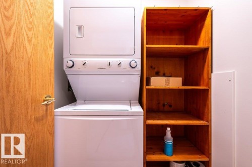 Stacked laundry appliances with adjacent wood shelving for excellent storage. - #203 8912 156 St Nw, Edmonton, AB 