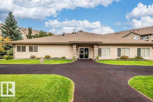 Stucco exterior with multiple windows, a divided light entry door, and a paved circular drive - #203 8912 156 St Nw, Edmonton, AB 