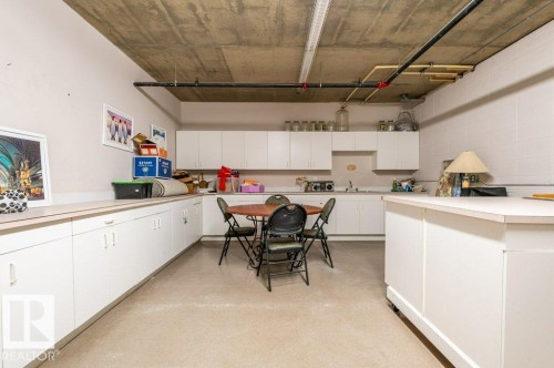 Extensive white cabinetry with a built-in sink, ample countertop space, a movable island, and exposed concrete ceiling - #203 8912 156 St Nw, Edmonton, AB 