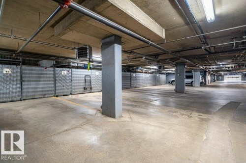 Underground parking facility featuring concrete flooring, exposed ceiling utilities, fluorescent lighting, and individual storage units.  A very well-kept and bright area. - #203 8912 156 St Nw, Edmonton, AB 
