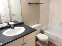 Vanity with an integrated sink and chrome faucet, dark speckled countertop, white cabinetry with dark hardware, full-width mirror, and a built-in tub with white tile surround - 
