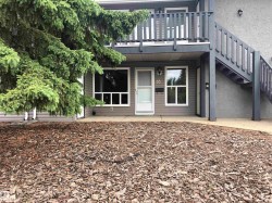 Upper-level balcony with wood railing, exterior staircase with wood railings, lower-level entry with storm door, ground-level windows with grid accents, and exterior wall sconce lighting - 