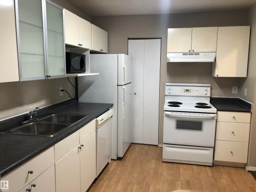 Kitchen featuring wood-finish flooring, dual basin stainless steel sink, flat-panel cabinetry, and white appliance package - #68 1503 Mill Woods Rd E Nw, Edmonton, AB 