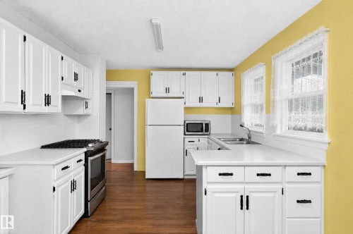 Kitchen featuring white cabinetry, white countertops, stainless steel range, and wood-finish flooring - 12309 80 Street Nw, Edmonton, AB 