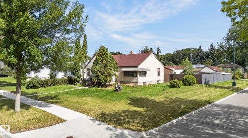 Corner lot property featuring mature trees, a red shingle roof, a light-toned exterior, and a well-maintained lawn - 12309 80 Street Nw, Edmonton, AB 