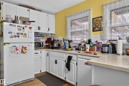 White cabinetry with dark hardware, dual windows, a white tile backsplash, wood-finish flooring, and light-toned countertops - 12309 80 Street Nw, Edmonton, AB 