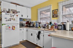 White cabinetry with dark hardware, dual windows, a white tile backsplash, wood-finish flooring, and light-toned countertops - 
