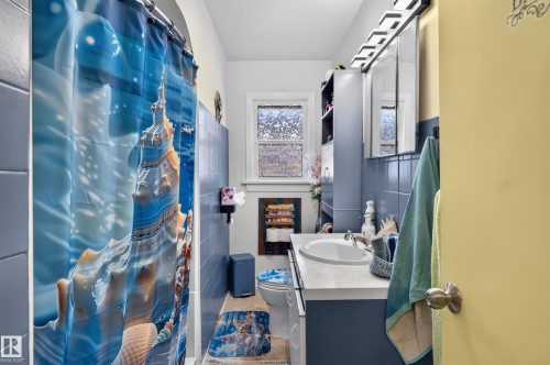 Full bathroom featuring a single vanity with an integrated sink, blue tile wainscoting, and a window with privacy glass - 12309 80 Street Nw, Edmonton, AB 