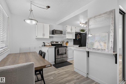 White cabinetry with brushed nickel hardware, stainless steel appliances, wood-finish flooring, recessed lighting, and a kitchen peninsula with a countertop - 130 Woodstock Nw, Edmonton, AB 