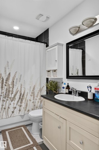 White vanity with dual cabinet doors and an undermount sink, dark countertop, and chrome faucet - 130 Woodstock Nw, Edmonton, AB 