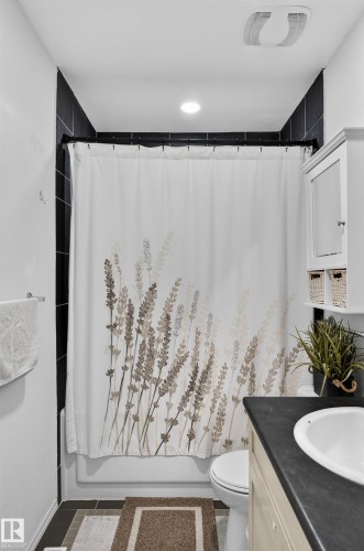 Tub/shower combination with black tile surround, white vanity with integrated sink, and wall-mounted storage cabinet - 130 Woodstock Nw, Edmonton, AB 
