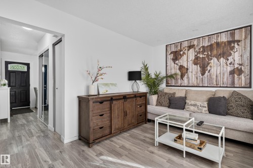 Wood-finish flooring throughout, white walls, and a recessed entryway with a dark paneled door featuring decorative glass - 130 Woodstock Nw, Edmonton, AB 