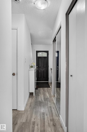 Wood-finish flooring, recessed lighting, white trim, mirrored closet doors, and black entry door with decorative glass - 130 Woodstock Nw, Edmonton, AB 