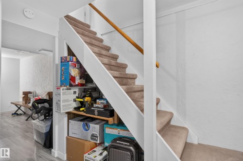 Carpeted stairs with a natural wood handrail, white risers, and a built-in storage shelf - 130 Woodstock Nw, Edmonton, AB 