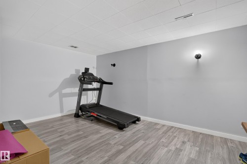 Spacious room with wood-finish flooring, drop ceiling, and wall sconce lighting - 130 Woodstock Nw, Edmonton, AB 