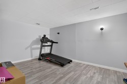 Spacious room with wood-finish flooring, drop ceiling, and wall sconce lighting - 