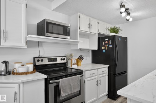 White cabinetry, stainless steel range, and light-toned countertops, complemented by a black refrigerator and track lighting - 130 Woodstock Nw, Edmonton, AB 