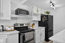 White cabinetry, stainless steel range, and light-toned countertops, complemented by a black refrigerator and track lighting - 