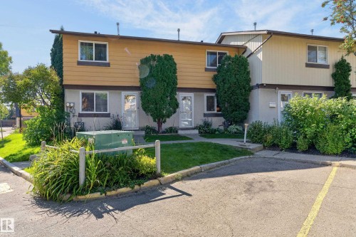 Two-story exterior with mixed siding, multiple entry doors, mature landscaping, and an asphalt parking area - 130 Woodstock Nw, Edmonton, AB 