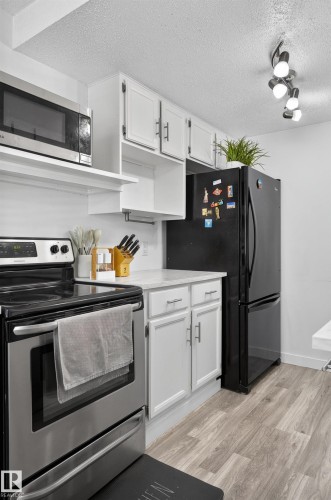 Stainless steel range, wood-finish flooring, white cabinetry with contemporary hardware, and track lighting - 130 Woodstock Nw, Edmonton, AB 