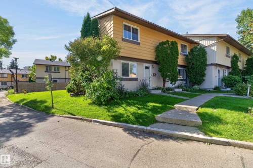 Duplex exterior with yellow siding and a partial brick facade, featuring a concrete walkway and a well-maintained lawn - 130 Woodstock Nw, Edmonton, AB 