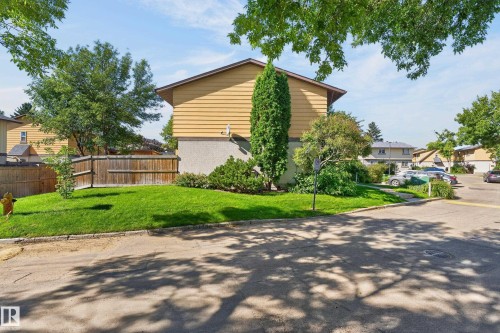Yellow siding exterior with a pitched roof, mature landscaping, and a well-maintained lawn - 130 Woodstock Nw, Edmonton, AB 