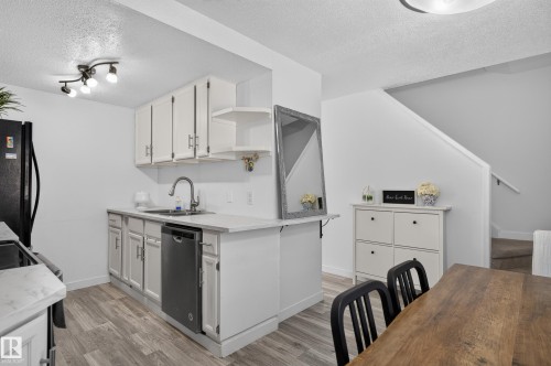 Kitchen featuring white cabinetry, stainless steel dishwasher, and wood-finish flooring - 130 Woodstock Nw, Edmonton, AB 