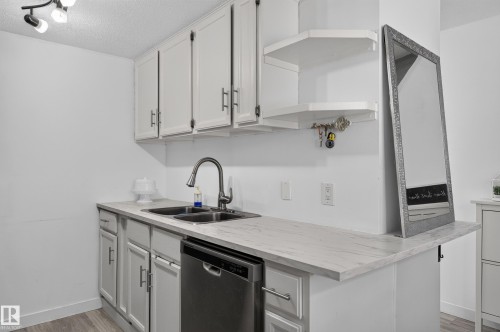White cabinetry with brushed nickel hardware, dual basin stainless steel sink, pull-down faucet, and a stainless steel dishwasher - 130 Woodstock Nw, Edmonton, AB 