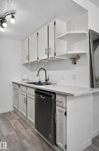 White cabinetry with modern hardware, integrated dishwasher, stainless steel sink with gooseneck faucet, light-toned countertop, and wood-finish flooring - 130 Woodstock Nw, Edmonton, AB 