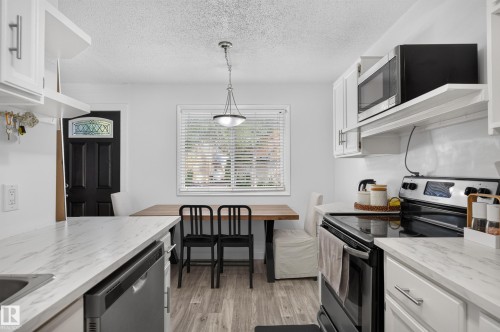 White cabinetry with brushed nickel hardware, light-toned wood-finish flooring, and a stainless steel dishwasher - 130 Woodstock Nw, Edmonton, AB 