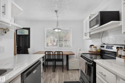 White cabinetry with brushed nickel hardware, light-toned wood-finish flooring, and a stainless steel dishwasher - 