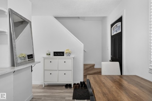 Wood-finish flooring with crisp white walls and a dark entry door featuring a decorative glass insert - 130 Woodstock Nw, Edmonton, AB 