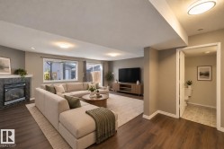 Spacious living area featuring wood-finish flooring, a fireplace with a stone surround, and recessed lighting - 