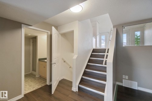 Wood-finish flooring, staircase with white risers, glass panel railing, and built-in vanity with countertop - 2117 36 Avenue Nw, Edmonton, AB 