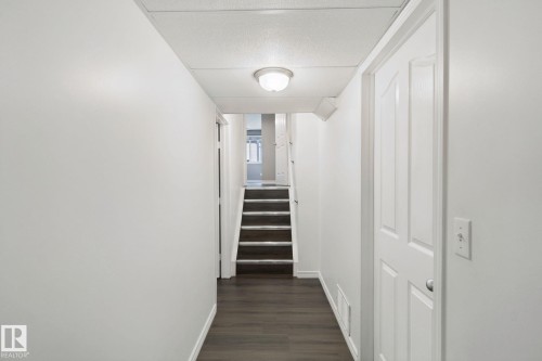 Hallway featuring dark wood-finish flooring, light-toned walls, a flush-mount ceiling light, and a paneled interior door - 2117 36 Avenue Nw, Edmonton, AB 