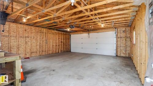 Spacious garage with exposed wood beam ceiling, concrete flooring, automatic garage door opener, and overhead lighting - 2117 36 Avenue Nw, Edmonton, AB 