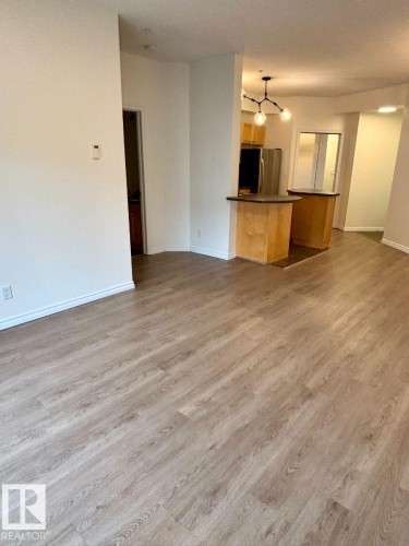 Expansive room featuring light-tone wood-finish flooring, white walls, and a modern ceiling light fixture - #103 10346 117 St Nw, Edmonton, AB 