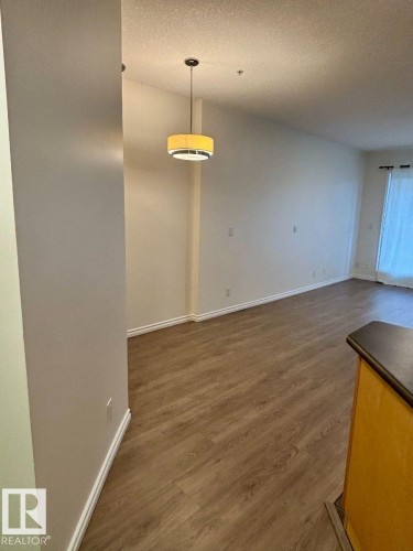 Wood-finish flooring throughout, white baseboards, pendant lighting fixture, and neutral wall tones - #103 10346 117 St Nw, Edmonton, AB 