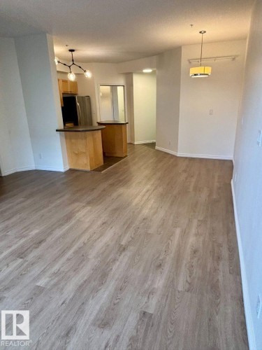 Light wood-finish flooring throughout, with a kitchen featuring wood cabinetry and stainless steel appliances - #103 10346 117 St Nw, Edmonton, AB 
