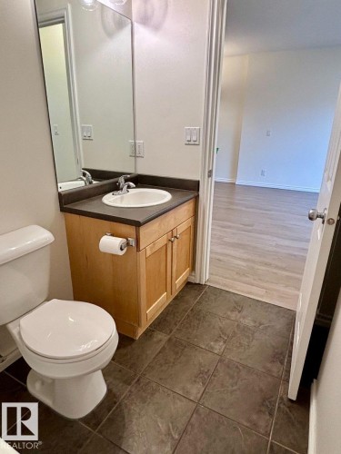 Bathroom featuring a single vanity with a laminate countertop, light wood-finish cabinetry, a ceramic drop-in sink, and a wall-mounted mirror - #103 10346 117 St Nw, Edmonton, AB 