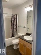 Bathroom with dark tile flooring, a built-in bathtub, a vanity with wood-finish cabinetry, a white basin sink, and an overhead vanity light fixture - 