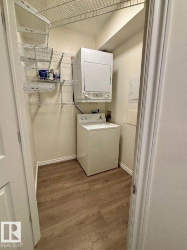 Dedicated laundry area with wood-finish flooring, white walls, and built-in wire shelving - #103 10346 117 St Nw, Edmonton, AB 