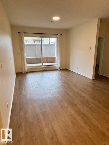 Wood-finish flooring throughout, sliding glass door leading to a private outdoor space, recessed lighting, and neutral wall tones - #103 10346 117 St Nw, Edmonton, AB 