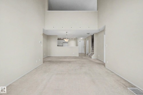 Soaring ceilings with recessed lighting, open loft area, kitchen passthrough with pendant lighting, and neutral carpeting throughout - #505 7839 96 St Nw, Edmonton, AB 