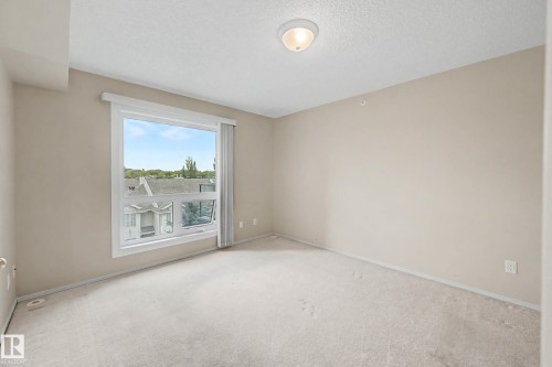 Light-colored wall-to-wall carpeting, neutral wall paint, and a large window with white framing - #505 7839 96 St Nw, Edmonton, AB 