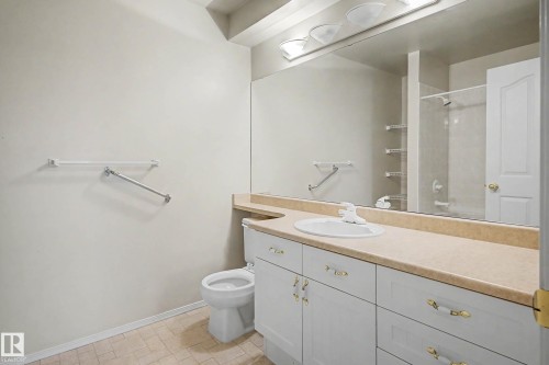 Bathroom featuring a vanity with a white basin sink, light-toned countertop, and white cabinetry with brass-finish hardware - #505 7839 96 St Nw, Edmonton, AB 