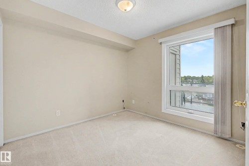 Wall-to-wall carpeting, neutral wall color, and a large window with vertical blinds - #505 7839 96 St Nw, Edmonton, AB 