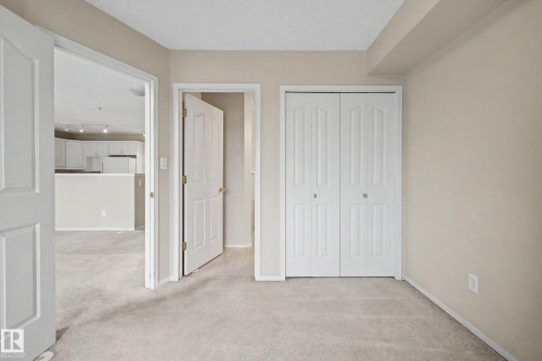Neutral tone wall color, light-colored carpet, white bi-fold closet doors, and white interior doors - #505 7839 96 St Nw, Edmonton, AB 