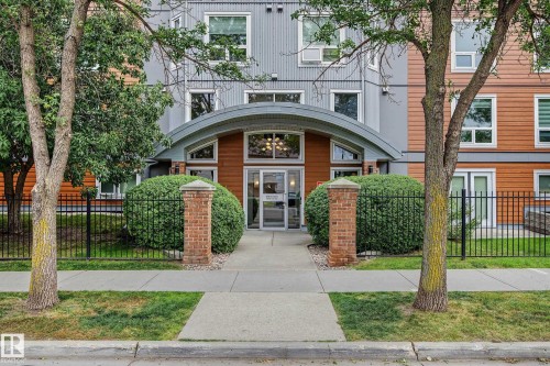Building exterior featuring modern gray and wood-finish siding, arched entrance canopy, and brick pillars - #505 7839 96 St Nw, Edmonton, AB 